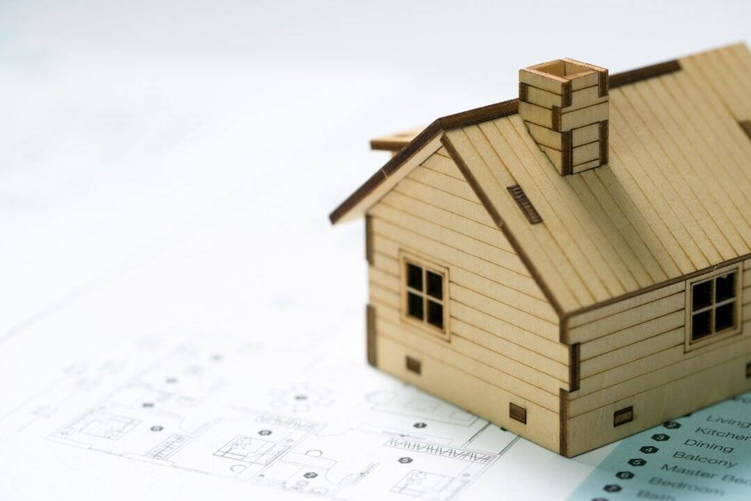 Small wooden house model on architectural blueprints, representing custom home construction and building design services.